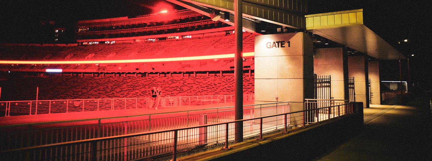 An empty stadium lit red at night, seen from the closed Gate 1 entrance